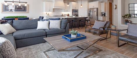 A modern living room with a grey sofa, a coffee table with a blue tray, and a dining area with a bar stool.