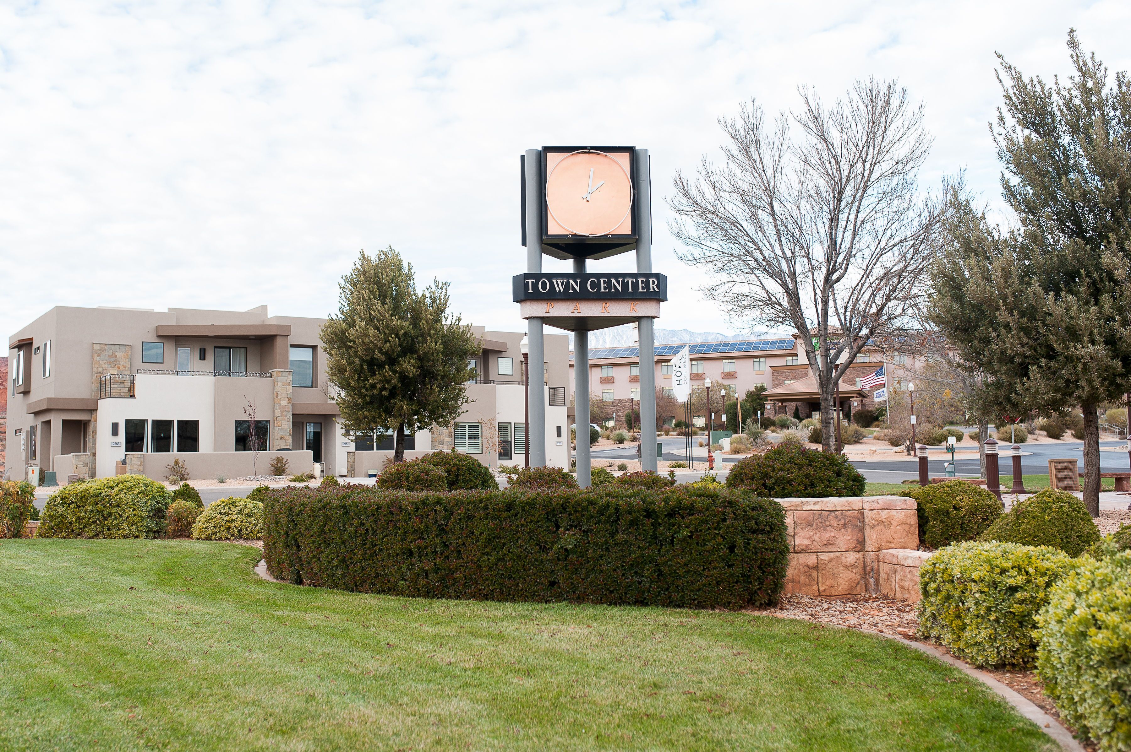 A clock tower with 'Town Center Park' sign, surrounded by well-maintained hedges and a grassy area.