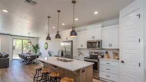 A modern kitchen with white cabinets, a central island with stools, stainless steel appliances, and pendant lighting.