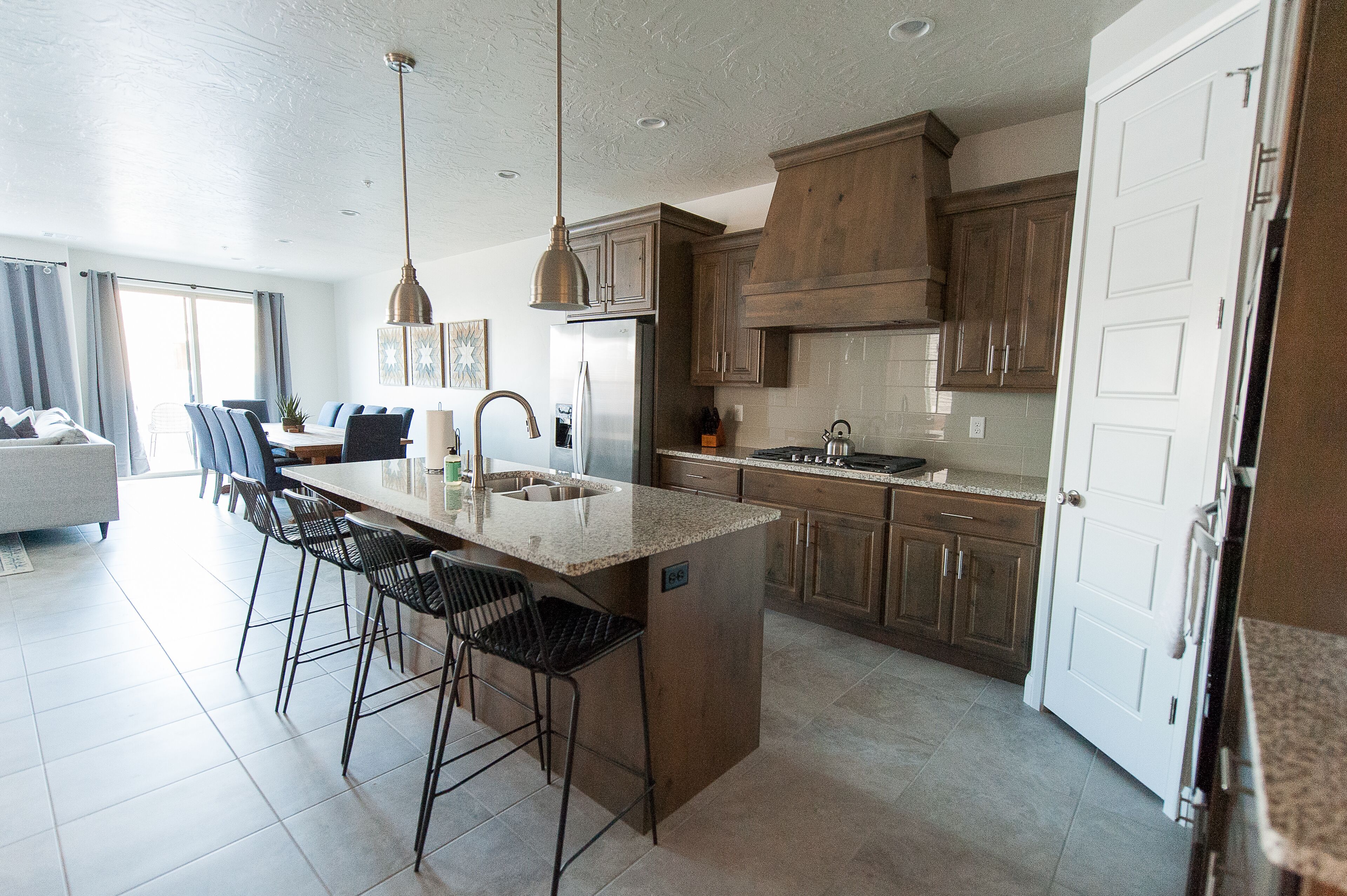 Una cocina moderna con una isla central, taburetes de bar, armarios de madera y un ventanal grande.