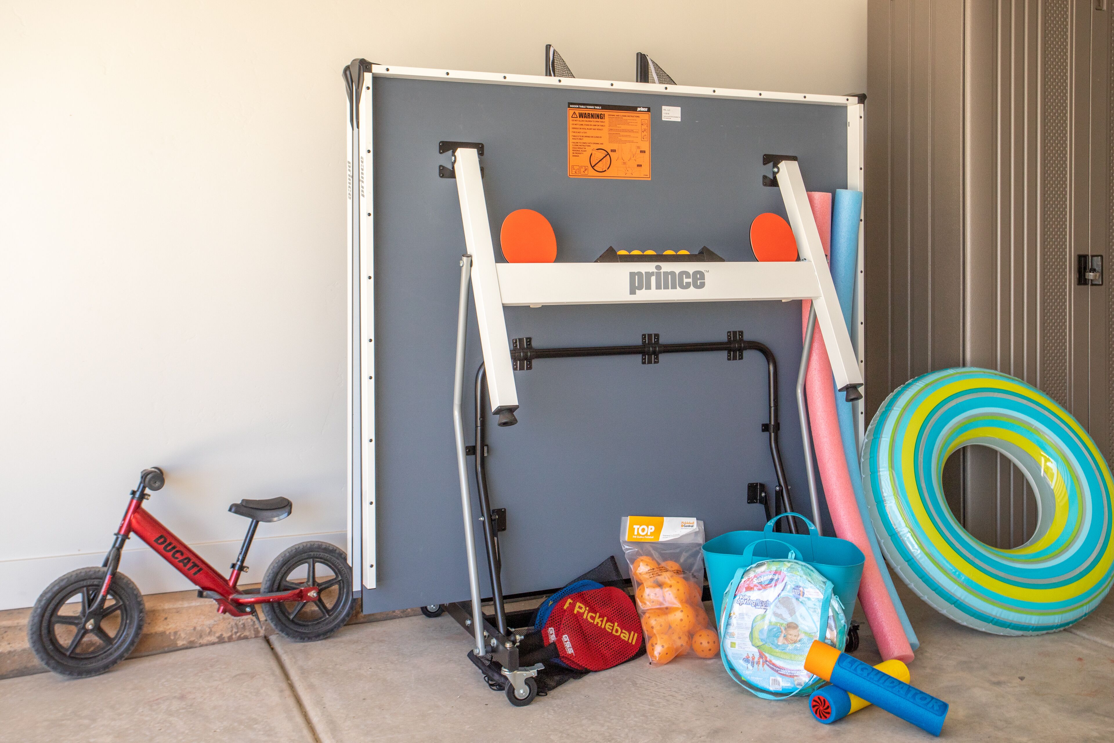 A room with a large storage unit, a red bicycle, a baby swing, a baby seat, and various toys and equipment.