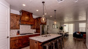 A spacious kitchen with wooden cabinets, a large island with bar stools, and pendant lighting.