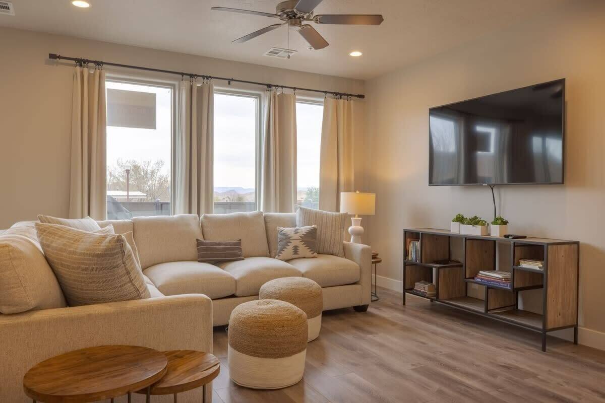 A living room with a sofa, ottomans, a coffee table, a TV, and a bookshelf.