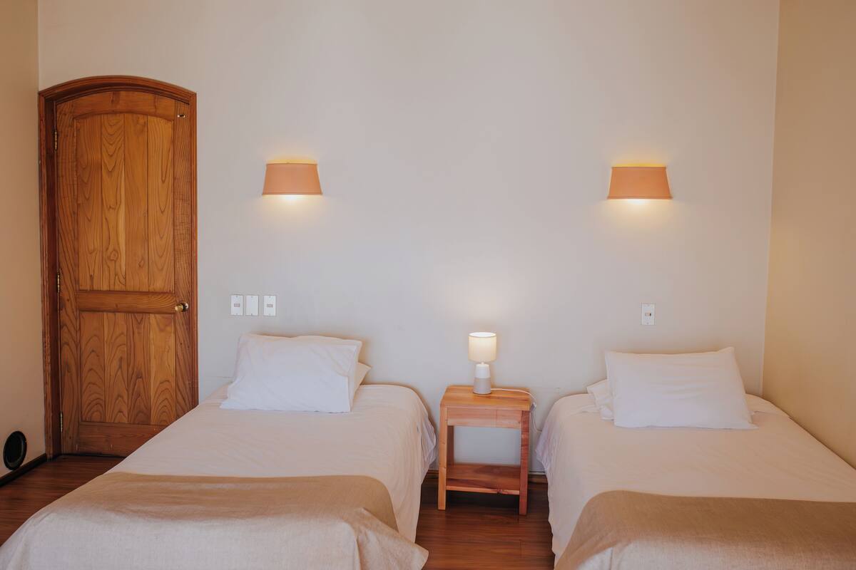 Una habitación con dos camas, una puerta de madera y dos lámparas fijadas a la pared.
