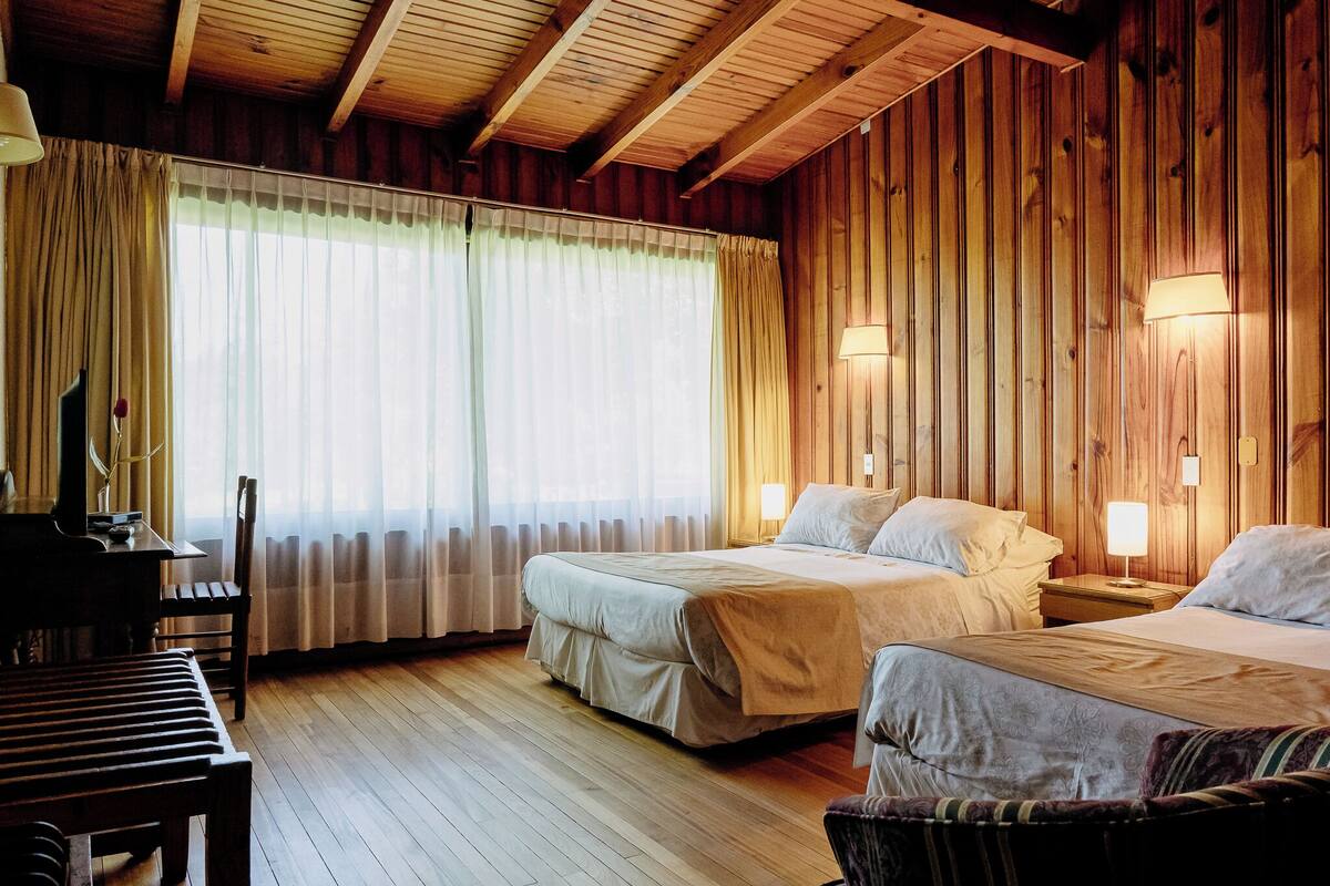 Una habitación con paneles de madera, dos camas, un escritorio y una silla.