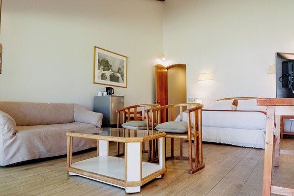 Una habitación acogedora con sofá, una mesa de centro de vidrio, sillas de madera, cama y espejo.