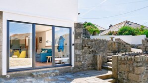 A modern house with a glass door leading to a living room with a blue sofa and yellow cushions. - Pipedream (Porthleven)