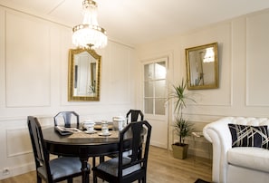 A dining area with a round table, black chairs, a chandelier, and a white couch with a patterned pillow.