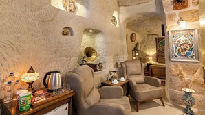 Une pièce chaleureuse aux murs de pierre, avec deux fauteuils confortables, une petite table en bois surmontée d’une lampe, une bouilloire et un réfrigérateur.