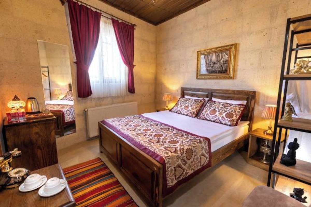 Een slaapkamer met een houten bed, een tapijt met rode en witte strepen, een nachtkastje van hout met een lamp en een spiegel.