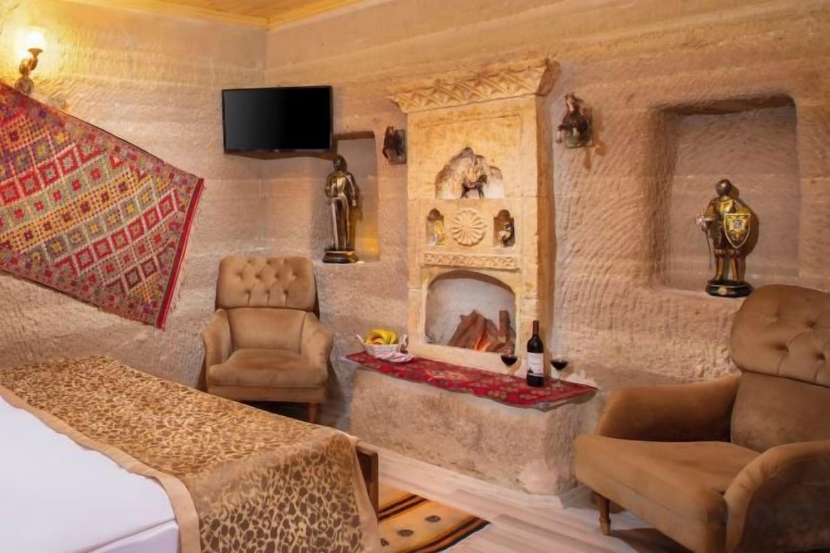 A room with a stone wall, a fireplace, a television, and two armchairs.