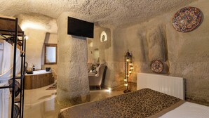 Une pièce comprenant un lit, un banc en bois, un miroir, un téléviseur et un mur décoré de motifs.