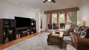 A living room with a flat-screen TV, a bookshelf, a coffee table, a sofa, and a patterned rug. - Location and Lifestyle at its Finest! (Naples)