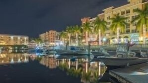 A marina with boats docked, a calm water body reflecting the buildings, and a row of palm trees. - Location and Lifestyle at its Finest! (Naples)