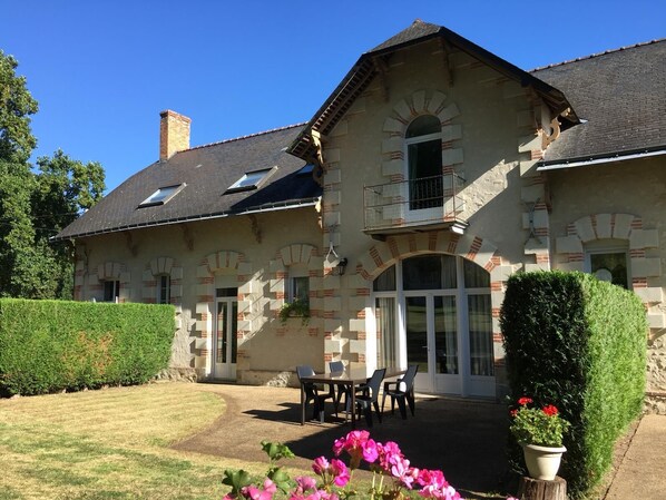 Ein großes Steinhaus mit einem geneigten Dach, zahlreichen Fenstern und einem Balkon.