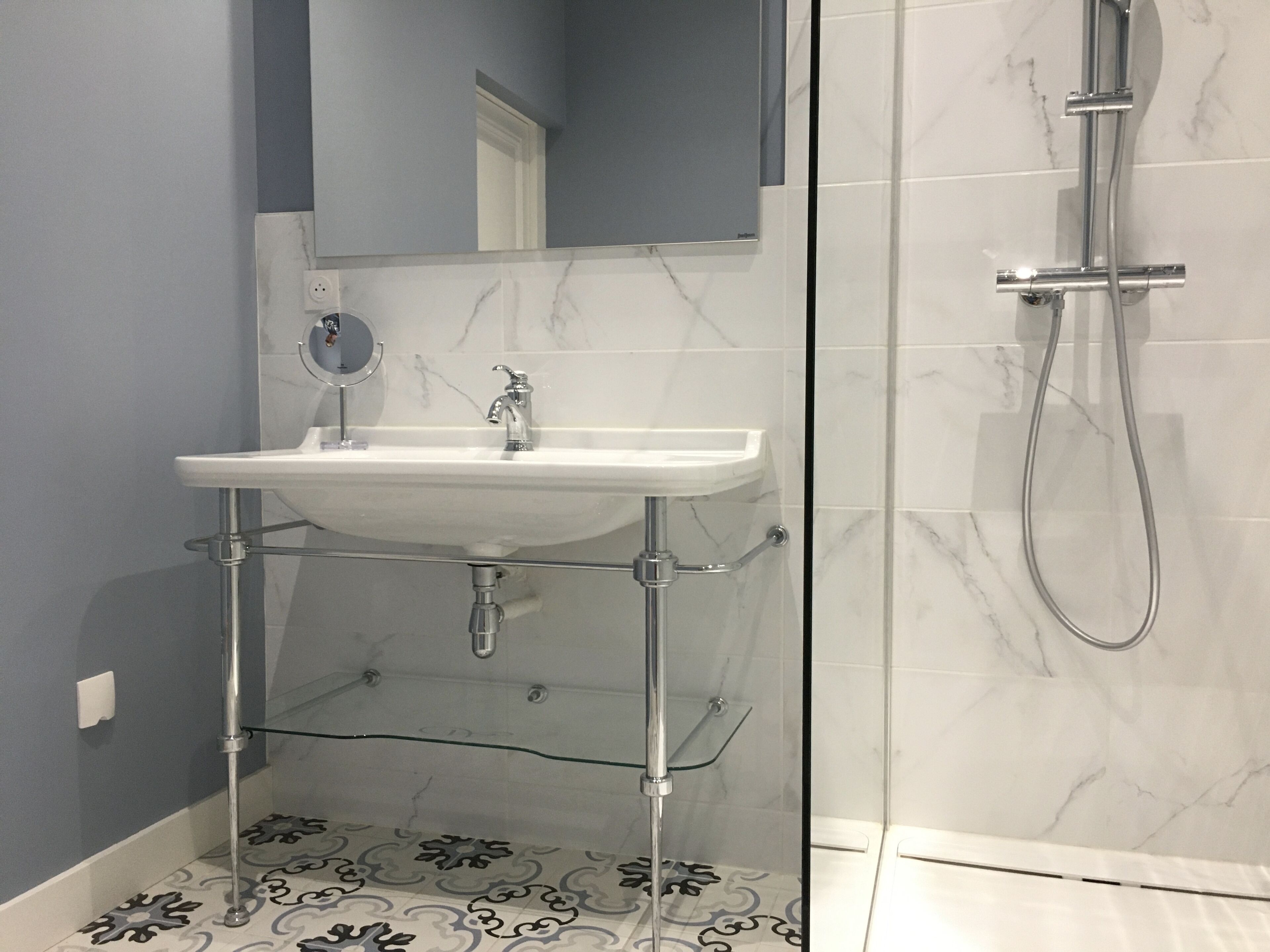 A bathroom with a white pedestal sink, a handheld showerhead, and a glass shower enclosure.