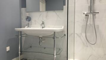 A bathroom with a white pedestal sink, a handheld showerhead, and a glass shower enclosure.