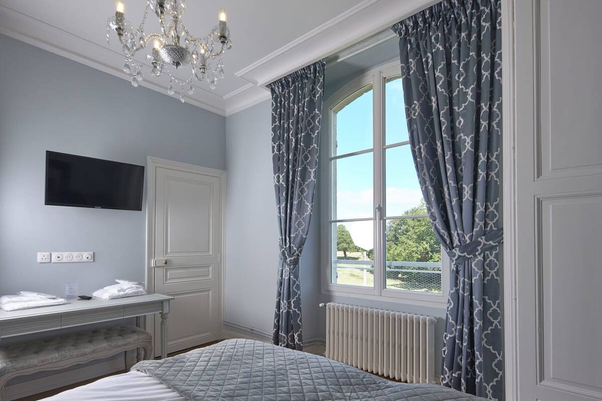A bedroom with a large bed, a desk, a TV, and a window with curtains.