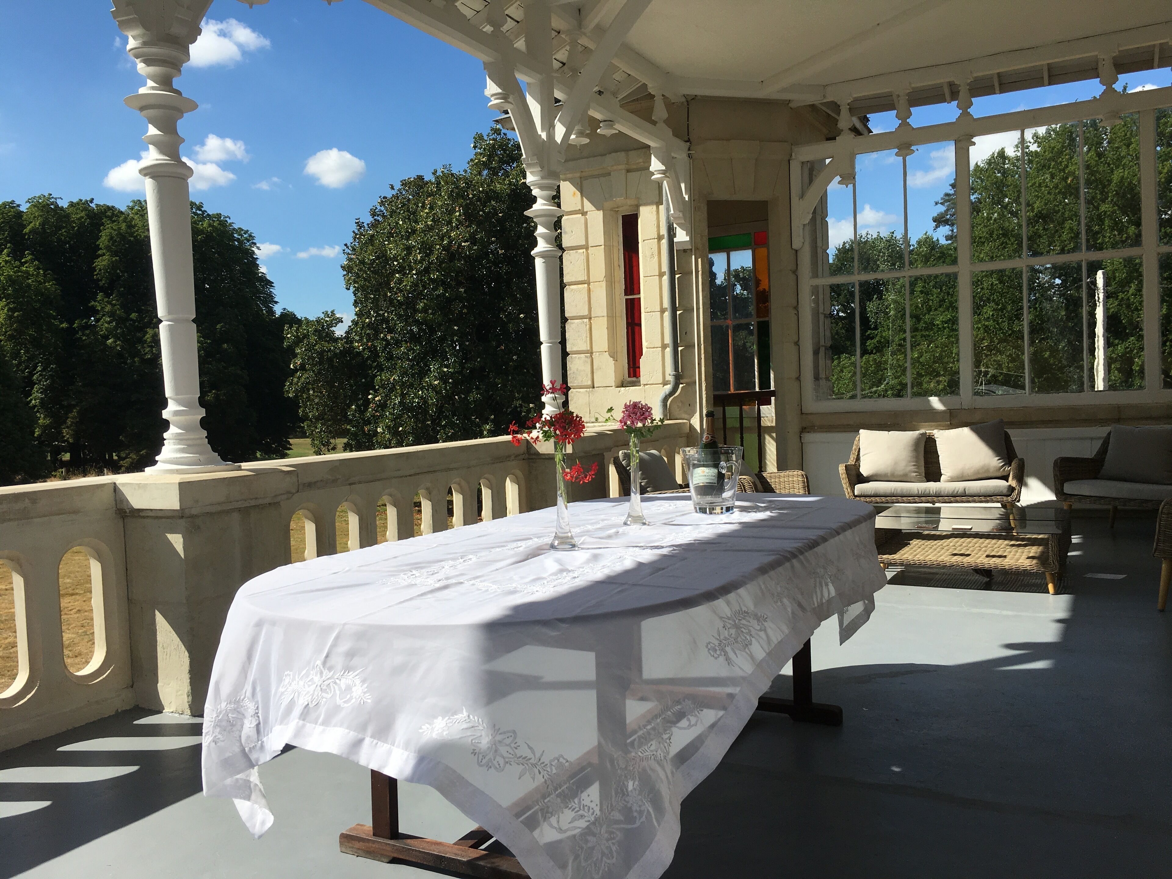 Un espacio al aire libre cubierto con una mesa preparada para dos personas, un florero con flores y una botella de champán.