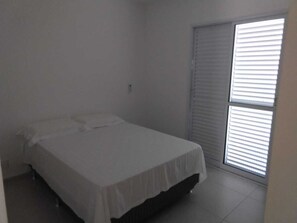 A small, clean bedroom with a single bed, a window with blinds, and a door.