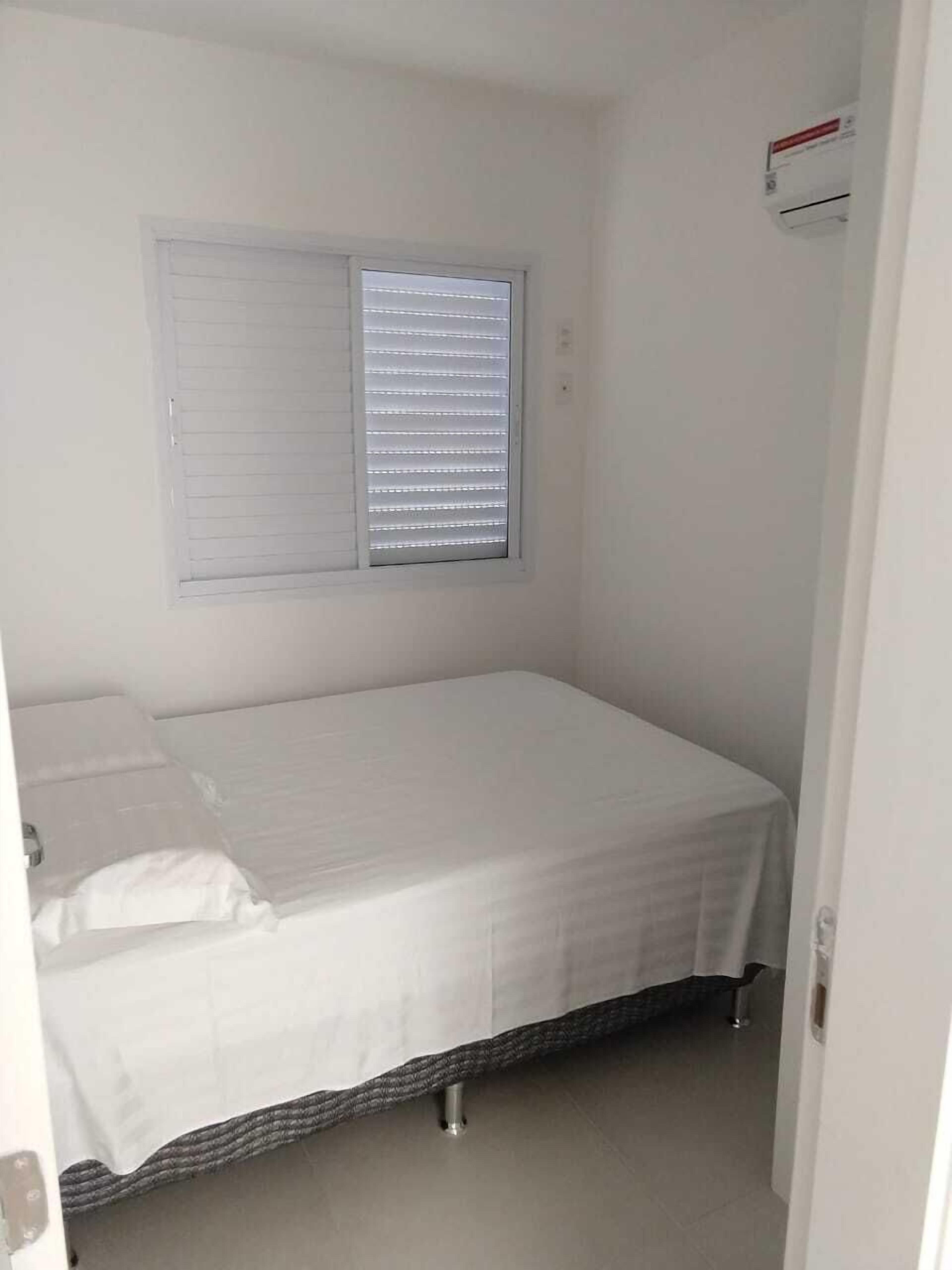 Une petite chambre avec un lit simple, une fenêtre et un appareil de climatisation fixé au mur.