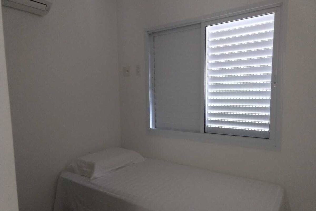 Ein kleines Zimmer mit einem Einzelbett, einem Fenster und einer Wand-Klimaanlage.