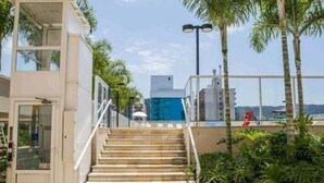 Ein modernes Gebäude mit einer Treppe, die zu einem Balkon führt, umgeben von Palmen und wolkenlosem Himmel.