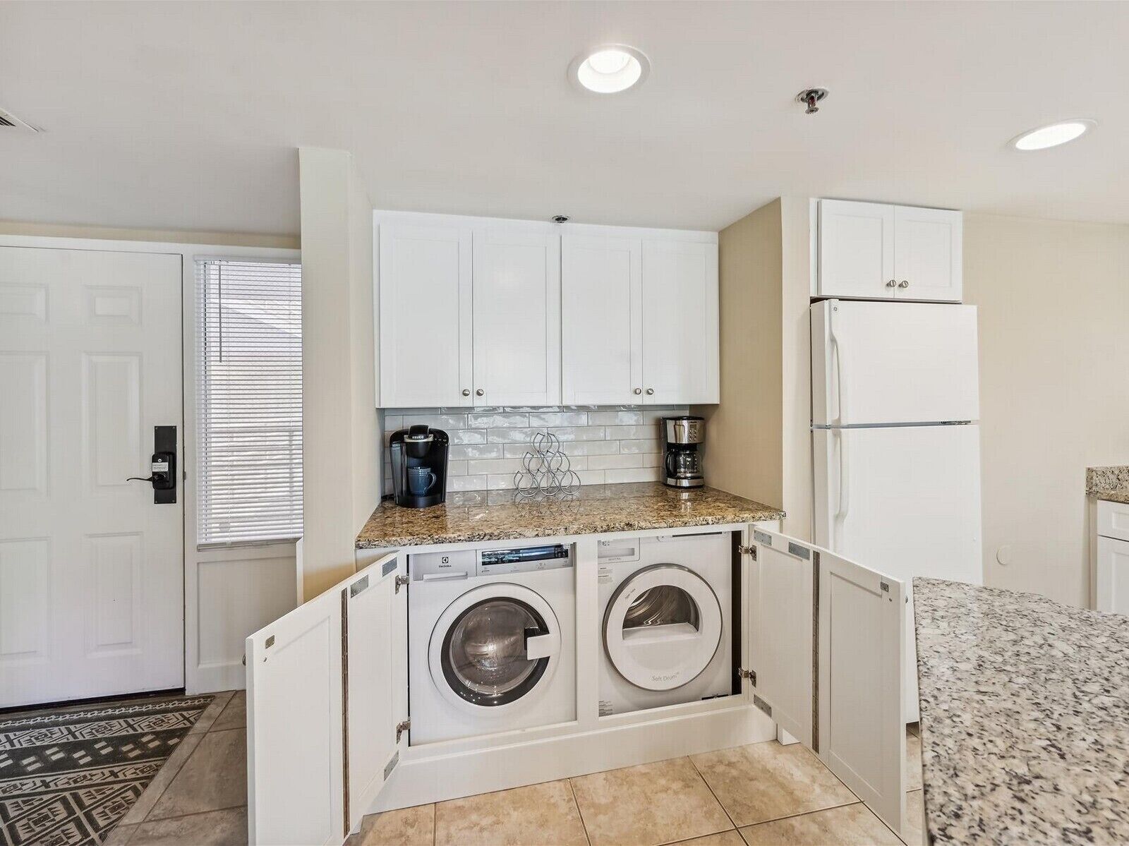 Cocina compacta con lavadora y secadora integradas, refrigerador y cafetera.