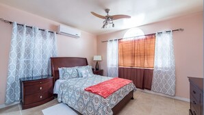 A bedroom with a bed, nightstands, a ceiling fan, an air conditioner, and a window with blinds. - Caicos Cactus Residence  Major Hill (Caicos Islands)