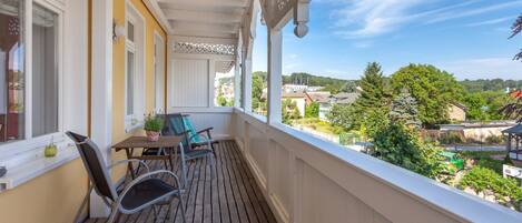 A balcony with wooden flooring, white railings, and a table with chairs.