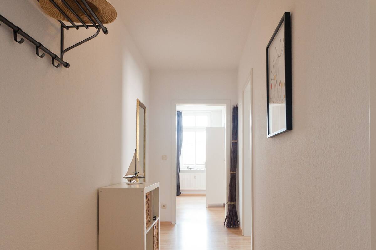 A hallway with wooden flooring, a white cabinet, a hat rack, and a framed picture on the wall.