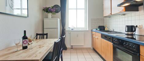 A kitchen with a wooden table, chairs, a refrigerator, a stove, and a window with curtains.
