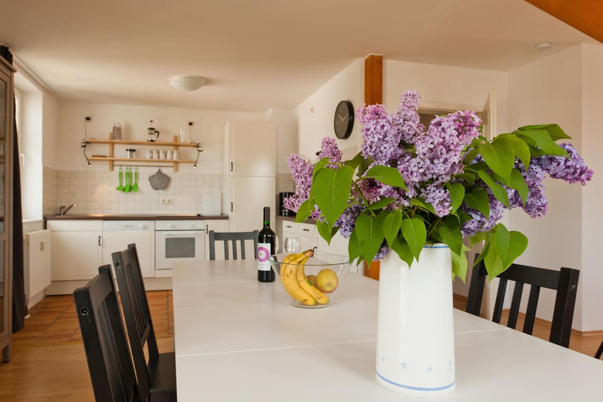 A dining table with a vase of flowers, a bottle of wine, and fruit.