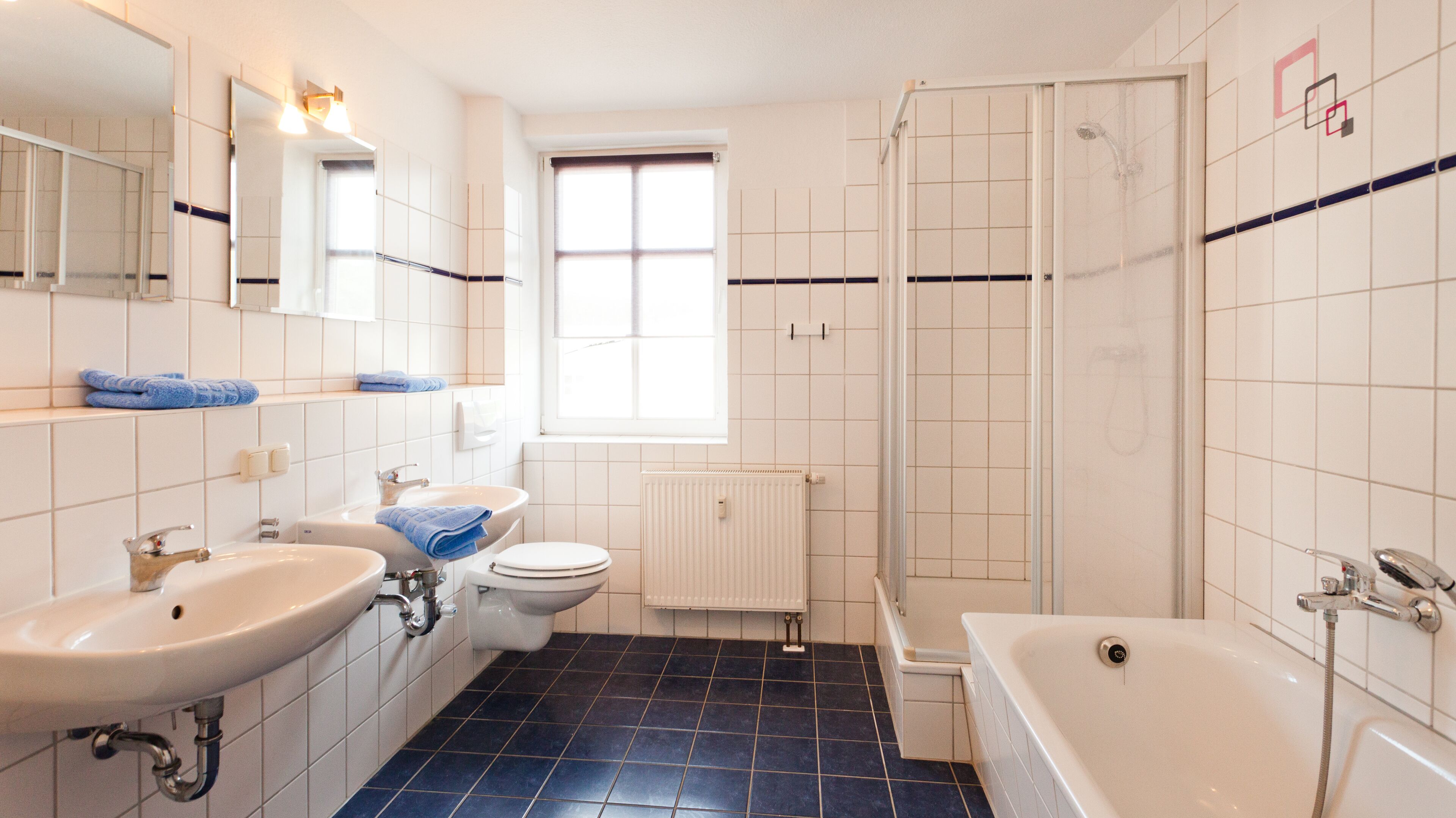 A bathroom with a white sink, toilet, and bathtub, a window, and a shower area.