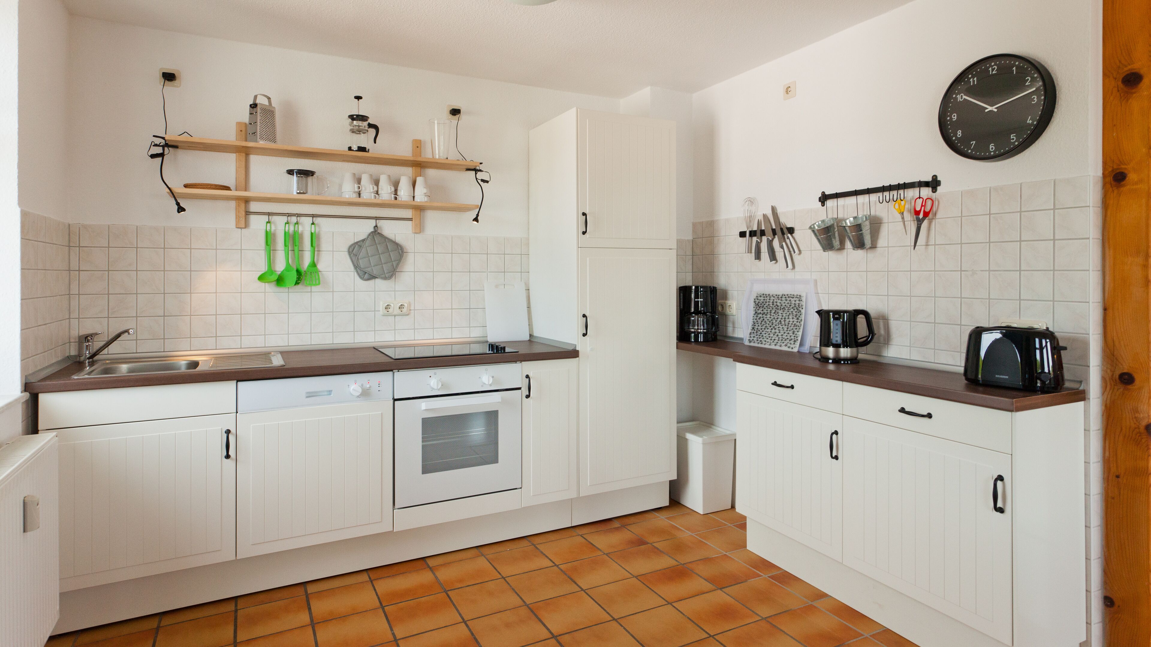 A kitchen with white cabinets, a wooden countertop, a coffee maker, a toaster, and various kitchen utensils on the wall.