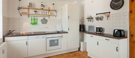 A kitchen with white cabinets, a wooden countertop, a coffee maker, a toaster, and various kitchen utensils on the wall.