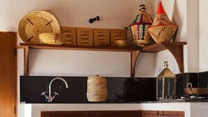 A rustic kitchen with wooden cabinets, a woven stool, and a round table. - Dar Rafti (Fes)