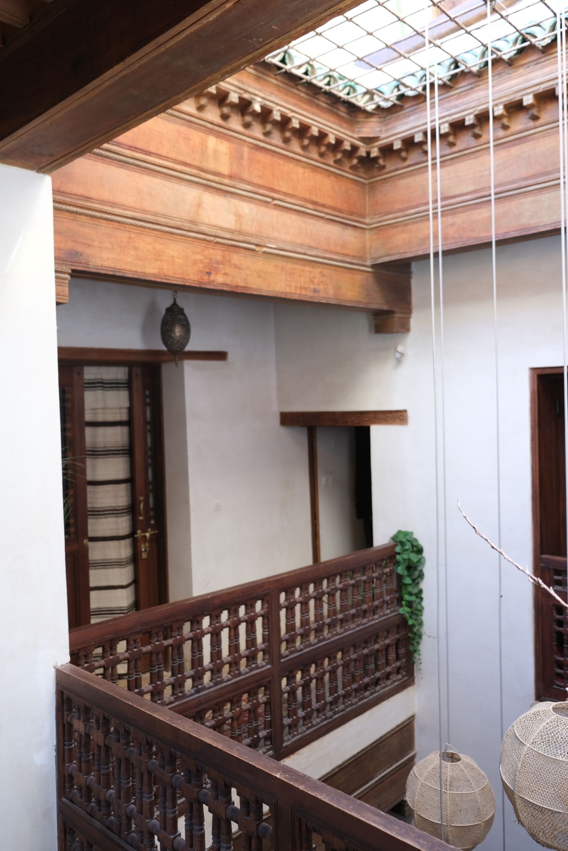 A traditional wooden balcony with a lattice railing, a hanging lantern, and a small potted plant.