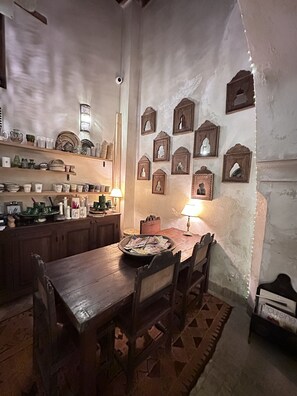 Zona de menjador rústica amb mobles de fusta, una taula amb revistes i prestatges amb utensilis de cuina.