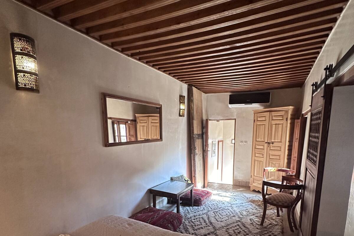 A bedroom with a bed, a small table, a chair, a mirror, and a wardrobe.