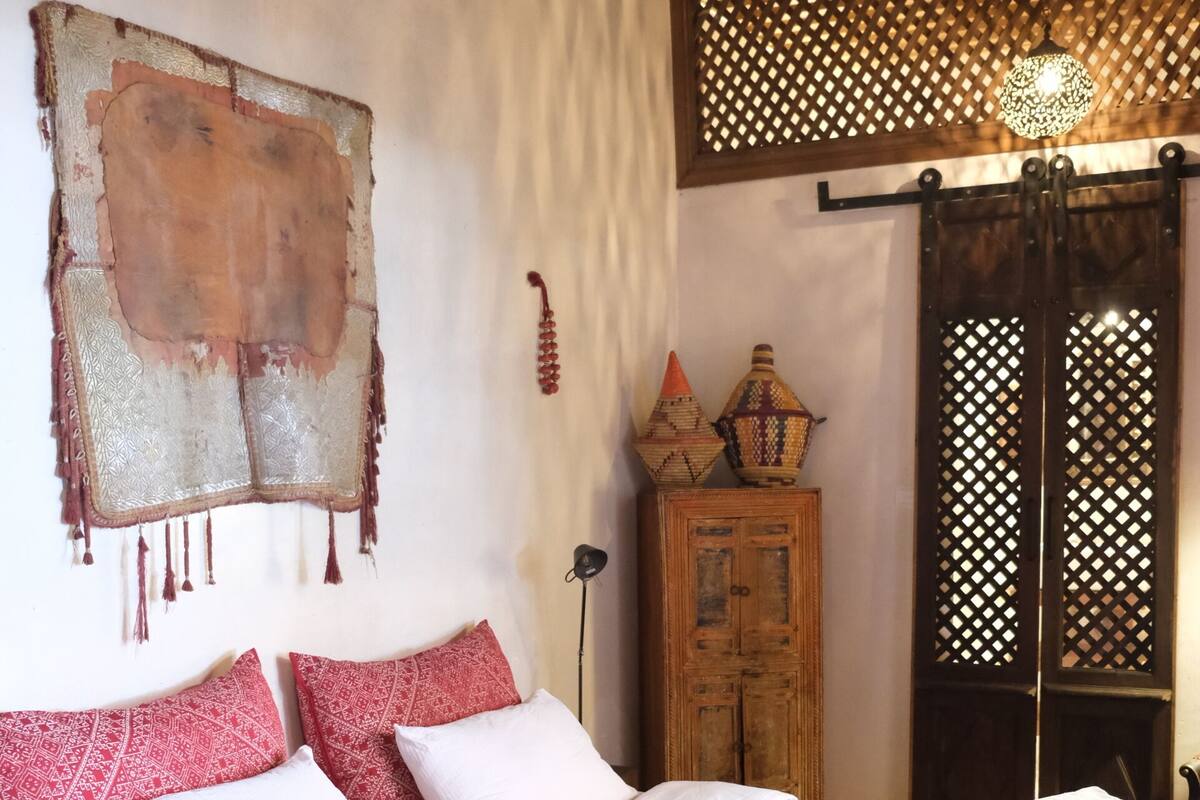 A bed with a red and white bedspread, a wooden cabinet, and a decorative wall hanging.