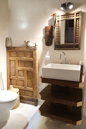Un bany amb una porta de fusta, un vàter blanc i un mirall amb una estructura decorativa.