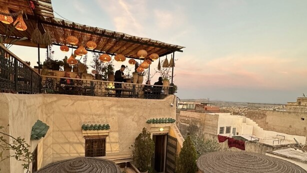 An outdoor seating area with tables and chairs, surrounded by potted plants and a thatched-roof structure. - Dar Rafti (Fes)
