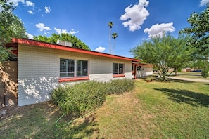 A single-story house with a red roof and white exterior walls, surrounded by a well-maintained lawn and a few trees.