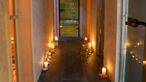 Un pasillo con una fila de velas encendidas en el suelo, que lleva a una puerta al final.