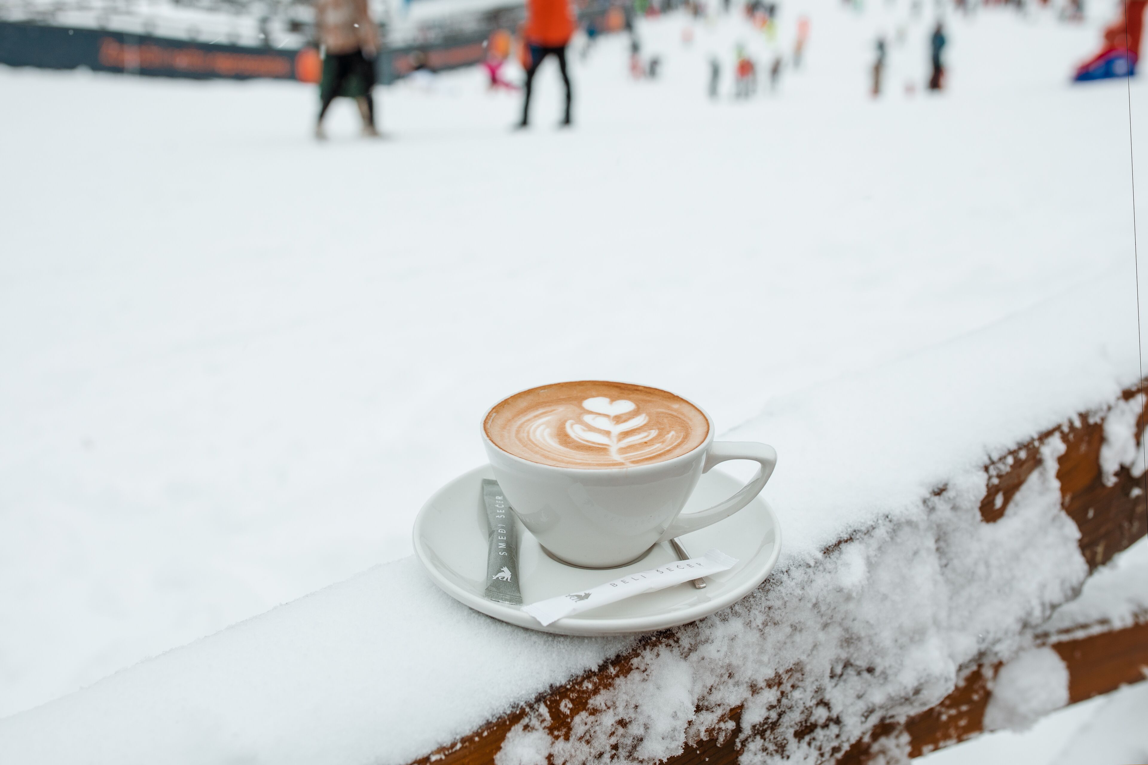 En kop kaffe med latte-kunst på en underkop, placeret på en snebelagt overflade.
