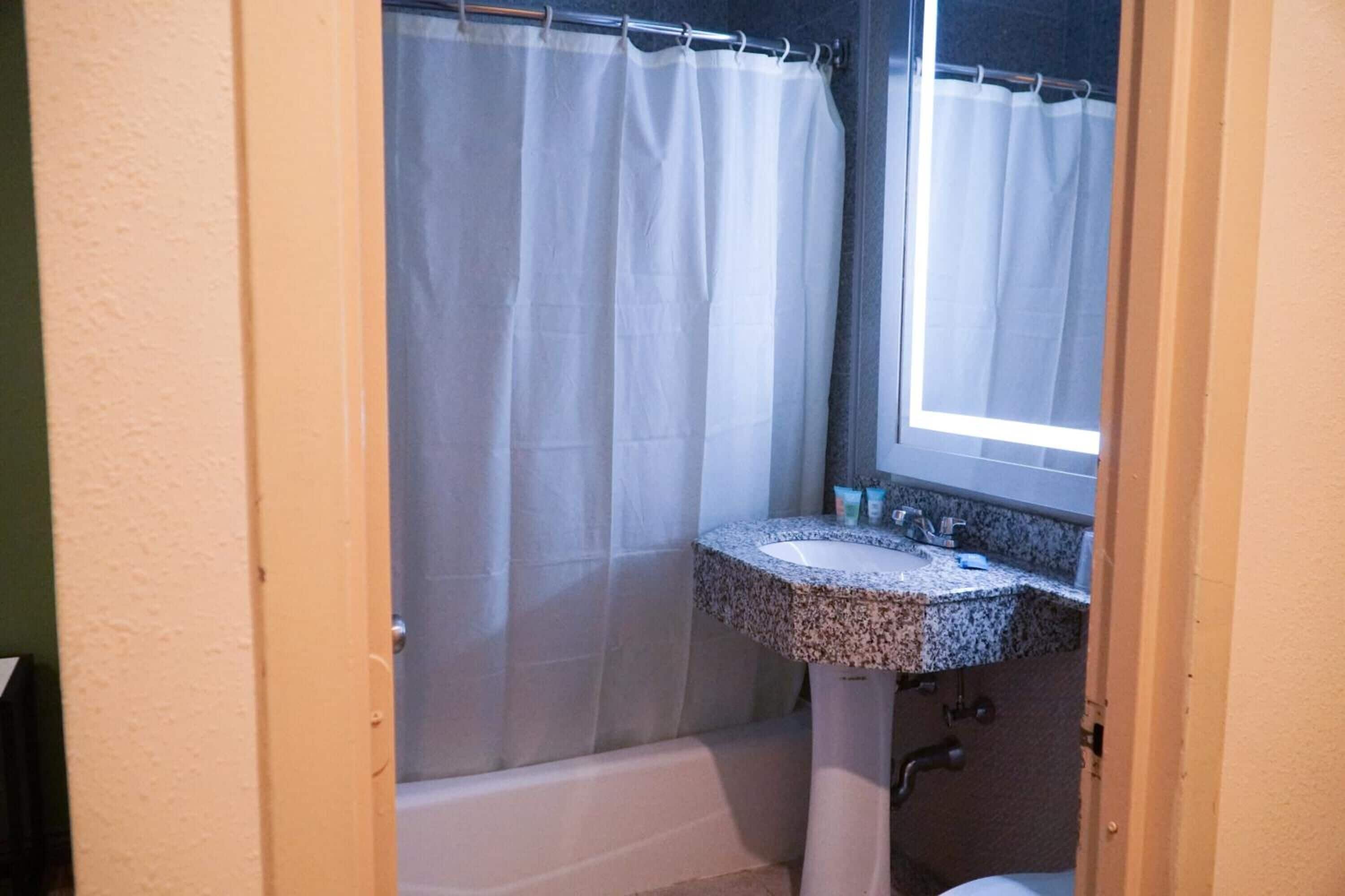Een badkamer met douchegordijn, wastafel en raam.