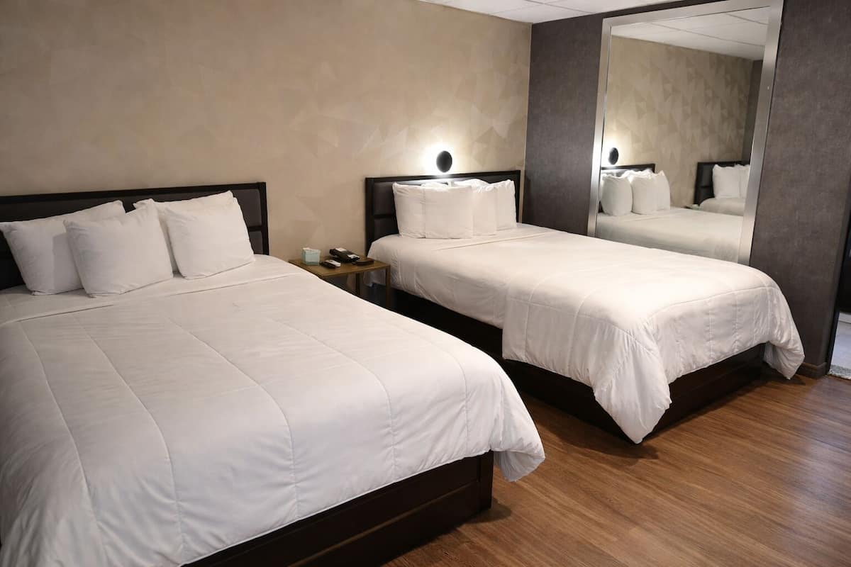 Una habitación de hotel con dos camas, una mesita de noche y un espejo grande.