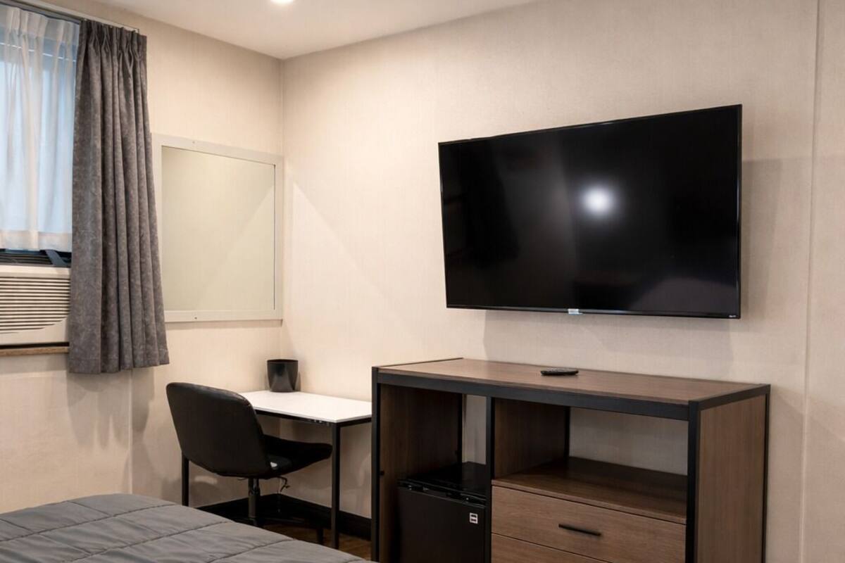 Una habitación de hotel con una cama, un escritorio, una silla, un televisor y un refrigerador pequeño.