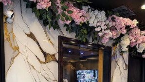 A reception desk with a marble wall, a mirror, and a decorative floral arrangement. - Cabana Hotel Yankee Stadium (Bronx)